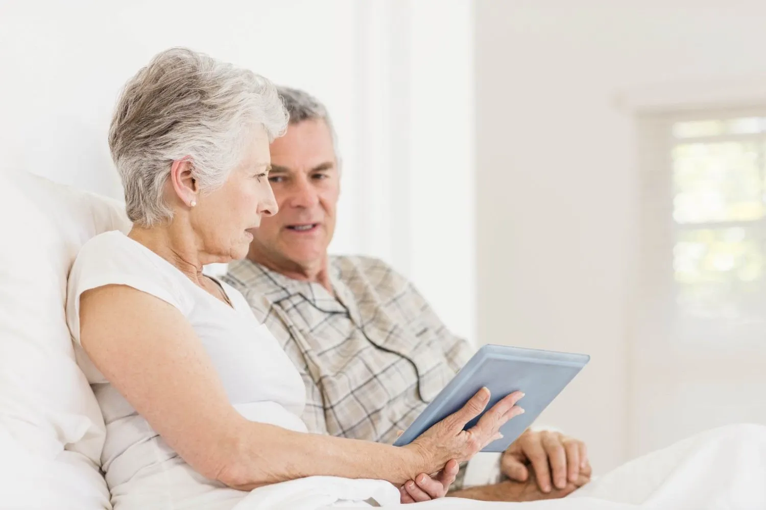 An older couple sitting up in bed looking at plan details on a tablet